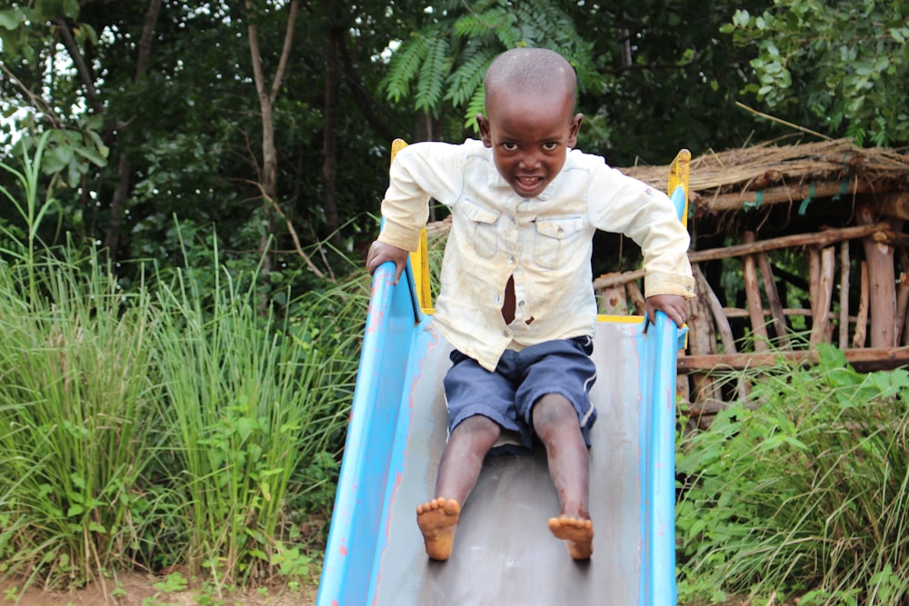 boy in yellow sweater and blue denim shorts sitting on blue slide during daytime