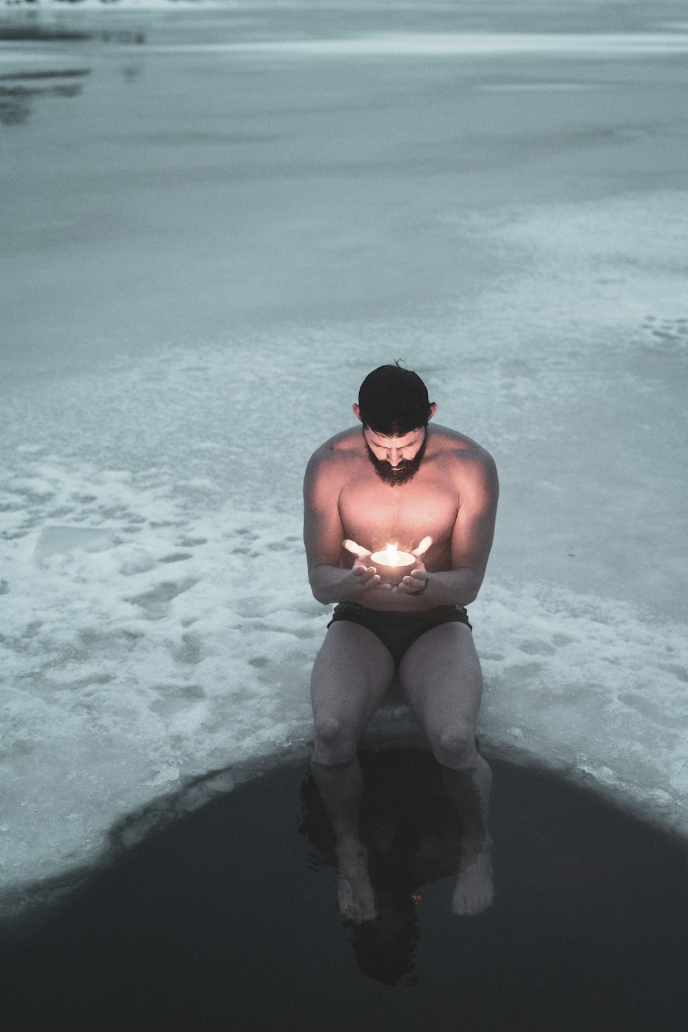 hombre en topless en pantalones cortos negros sentado en roca negra en el mar