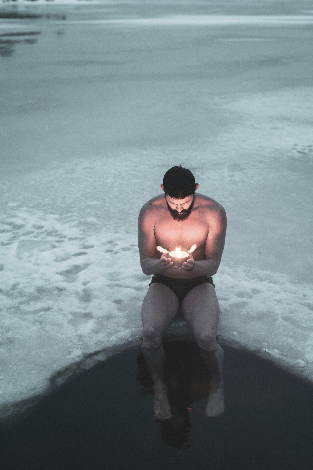 topless man in black shorts sitting on black rock in the sea