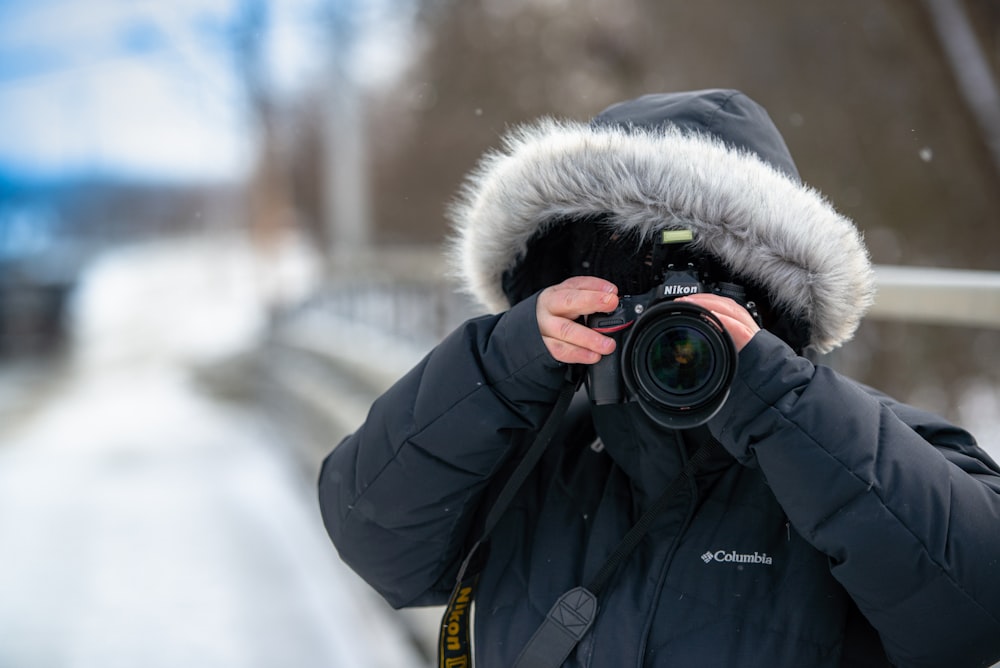 person in black and white parka jacket holding black dslr camera