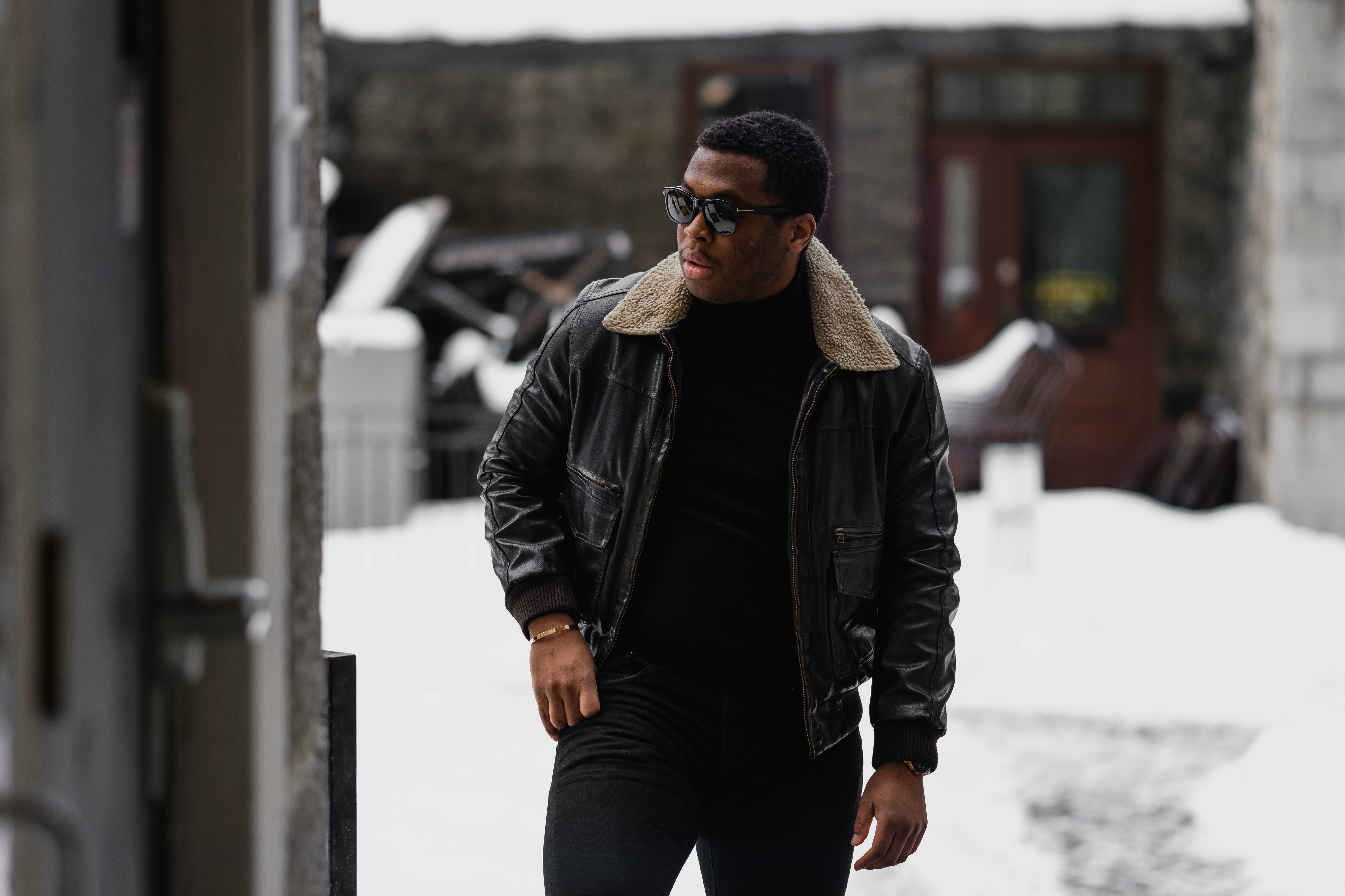man in black leather jacket and black pants standing on snow covered ground during daytime
