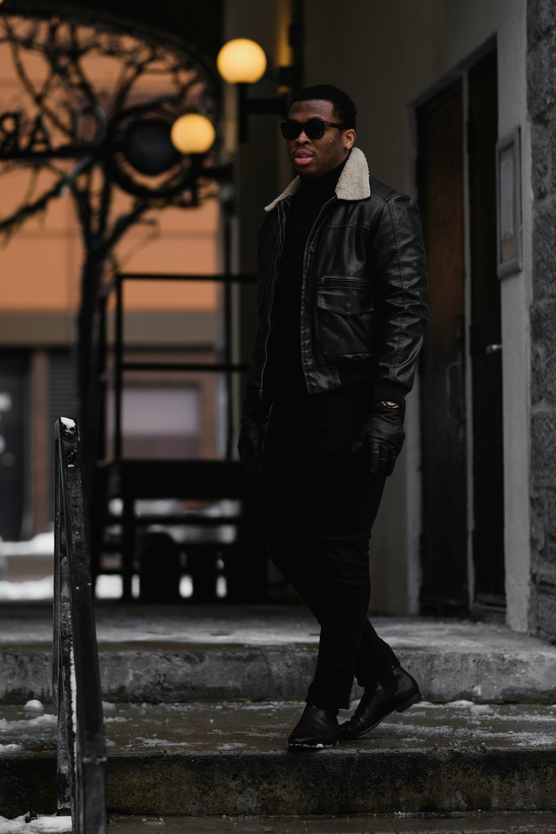 man in black leather jacket and black pants standing on sidewalk during daytime