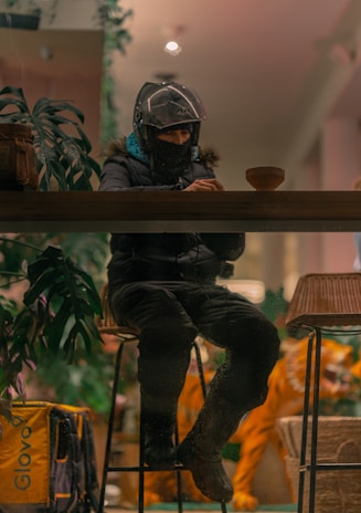 man in black jacket wearing helmet sitting on brown wooden table