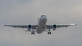 An airplane is captured mid-flight, in a clear sky with its landing gear extended. The perspective is from directly in front, showcasing the symmetry of the aircraft's wings and engines.