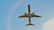 A commercial airplane is captured mid-flight from underneath, soaring through a clear blue sky. The aircraft appears sleek and modern, with visible jet engines and a distinct tail fin.