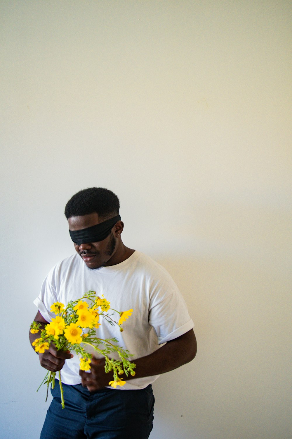 homme en t-shirt à col rond blanc tenant un bouquet de fleurs jaunes