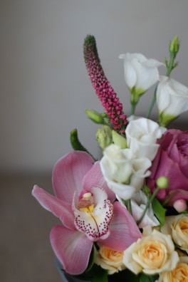 A beautifully arranged bouquet featuring a variety of flowers including pink orchids, white lisianthus, and small yellow roses. Detailed textures and soft petals create a delicate and elegant composition.
