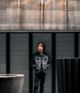Model wearing layered industrial outdoor gear standing against a backdrop of rocky terrain and deep iron gray skies