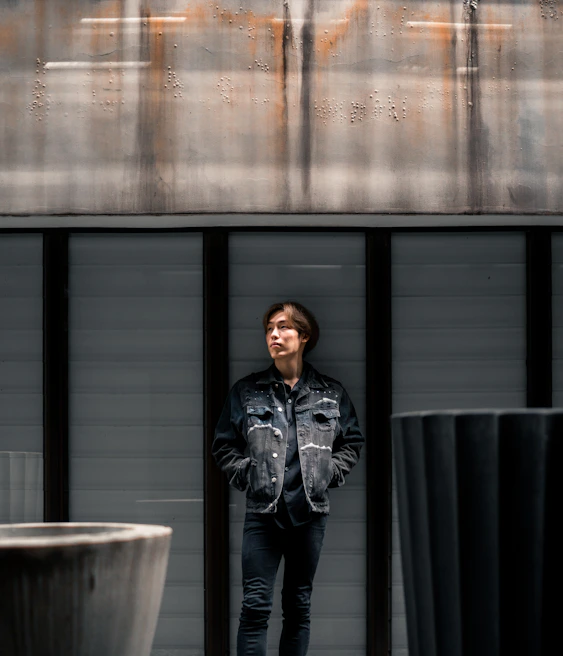 Model wearing layered industrial outdoor gear standing against a backdrop of rocky terrain and deep iron gray skies