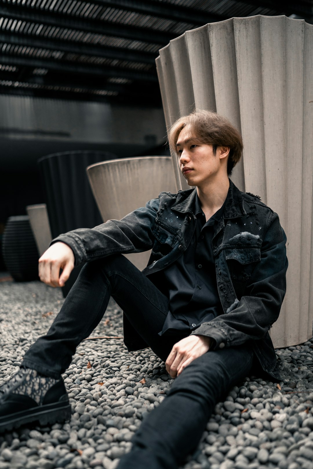 man in black leather jacket and black pants sitting on gray concrete floor