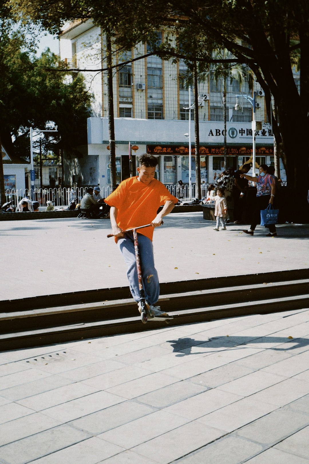 man in orange t-shirt and blue denim jeans walking on sidewalk during daytime