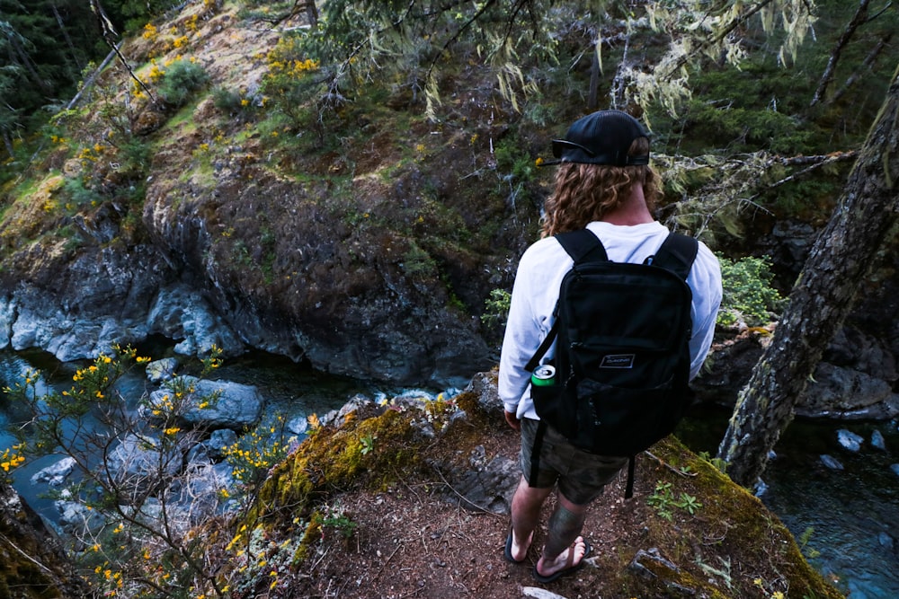 man in white shirt and black backpack standing on rocky ground