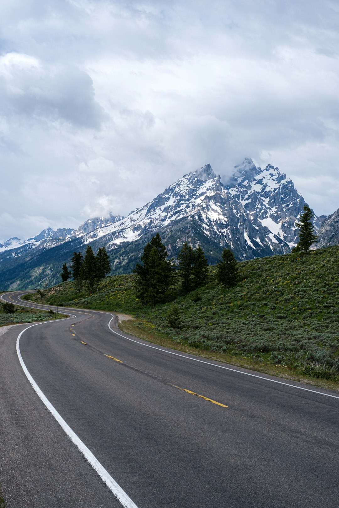 gray concrete road near green trees and mountain under white clouds during daytime