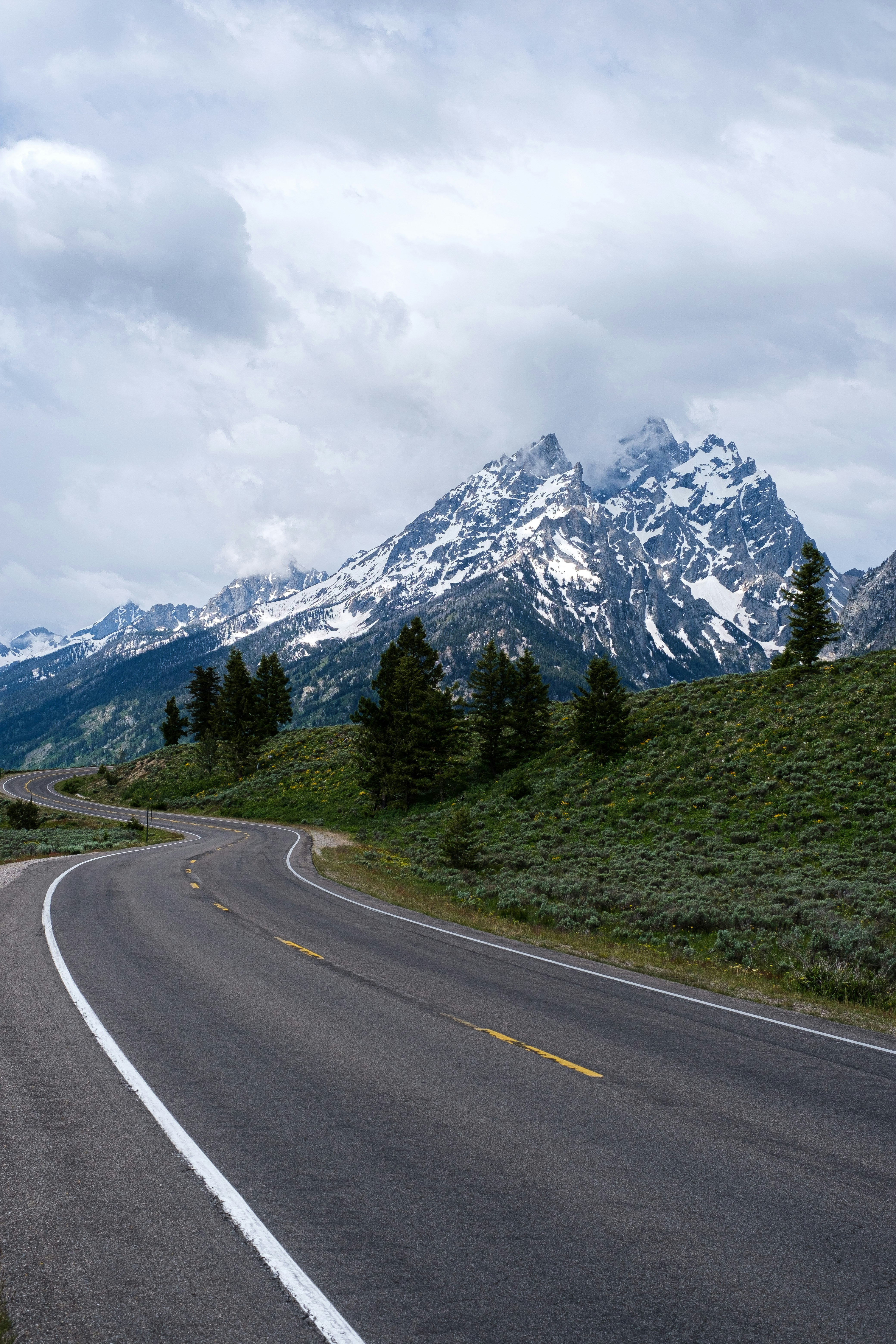 gray concrete road near green trees and mountain under white clouds during daytime