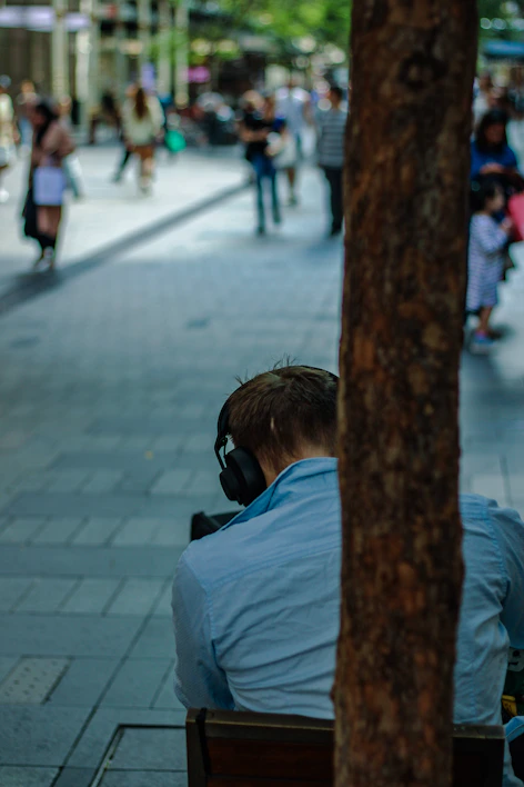 A cozy traveler listening to an audio guide on headphones in a historic city square.