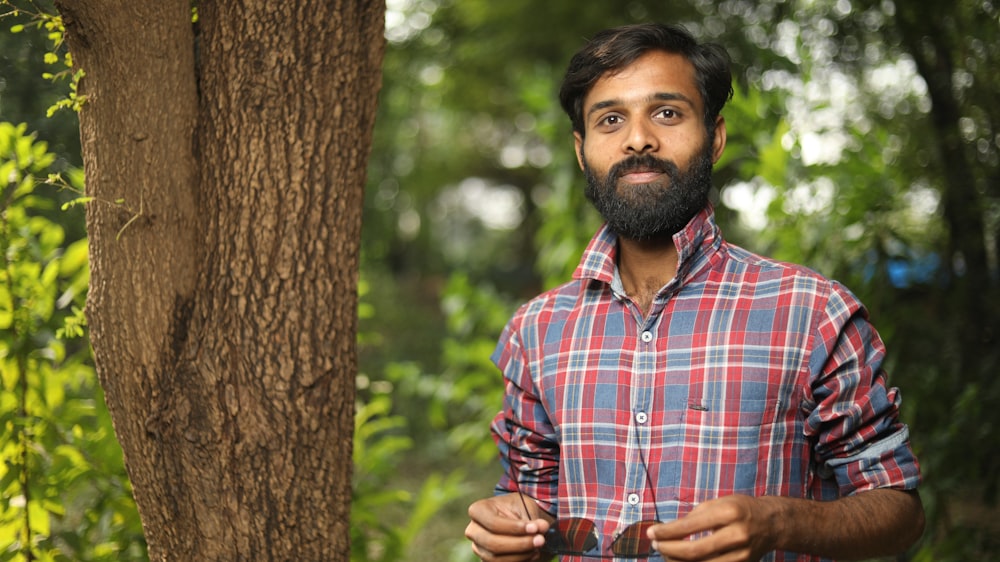 man in blue and red plaid dress shirt standing beside brown tree during daytime