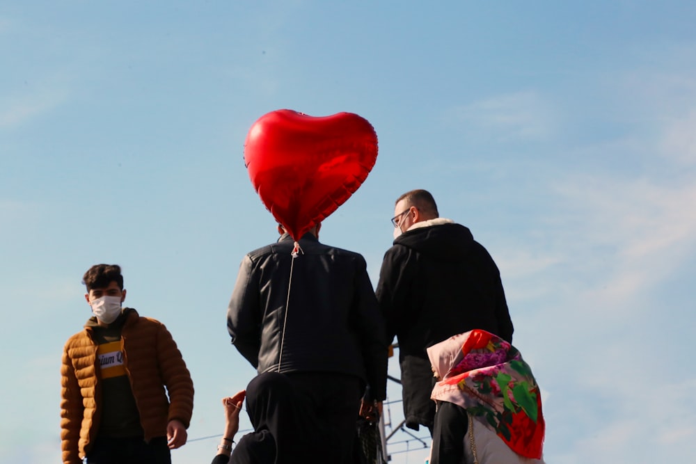 man in black coat holding red balloon