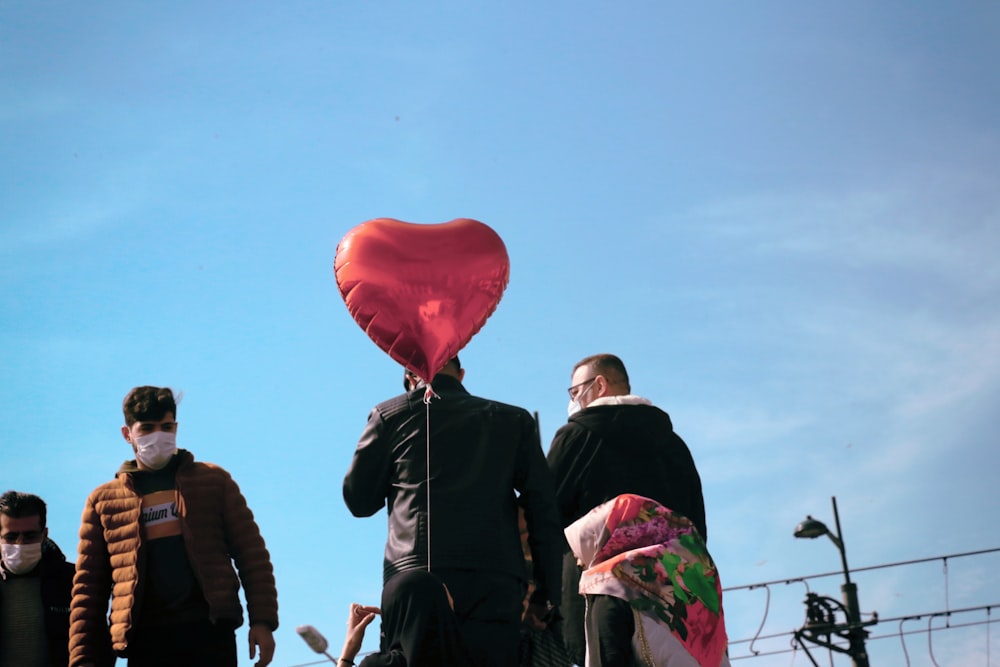 man in black jacket holding red balloon