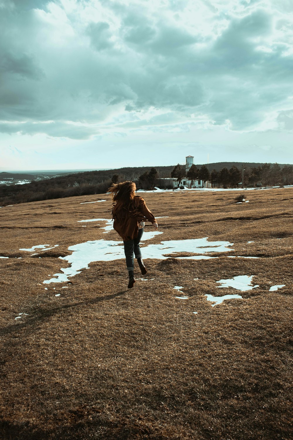 woman in brown coat walking on brown field during daytime