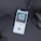 A smartphone displaying an audiobook app screen with a cover titled 'Aum Golly' and subtitle 'The Poem About the Origins of Man.' The phone is on a dark surface with a pair of headphones and a microphone visible nearby. The image composition suggests a podcast or audiobook listening setup.