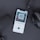 A smartphone displaying an audiobook app screen with a cover titled 'Aum Golly' and subtitle 'The Poem About the Origins of Man.' The phone is on a dark surface with a pair of headphones and a microphone visible nearby. The image composition suggests a podcast or audiobook listening setup.