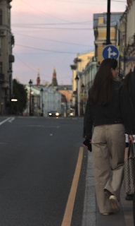 A person wearing a modern crossbody bag walking along a bustling city street at sunset