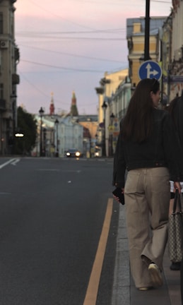 A stylish woman carrying a sleek tote bag on a city street at sunset.