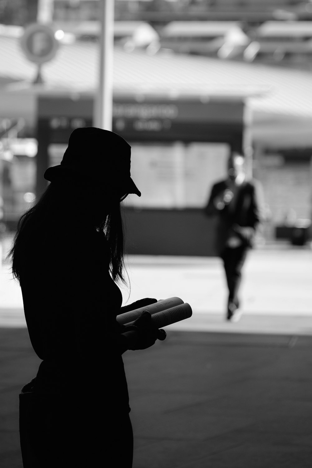 grayscale photo of woman in black hat and coat holding smartphone
