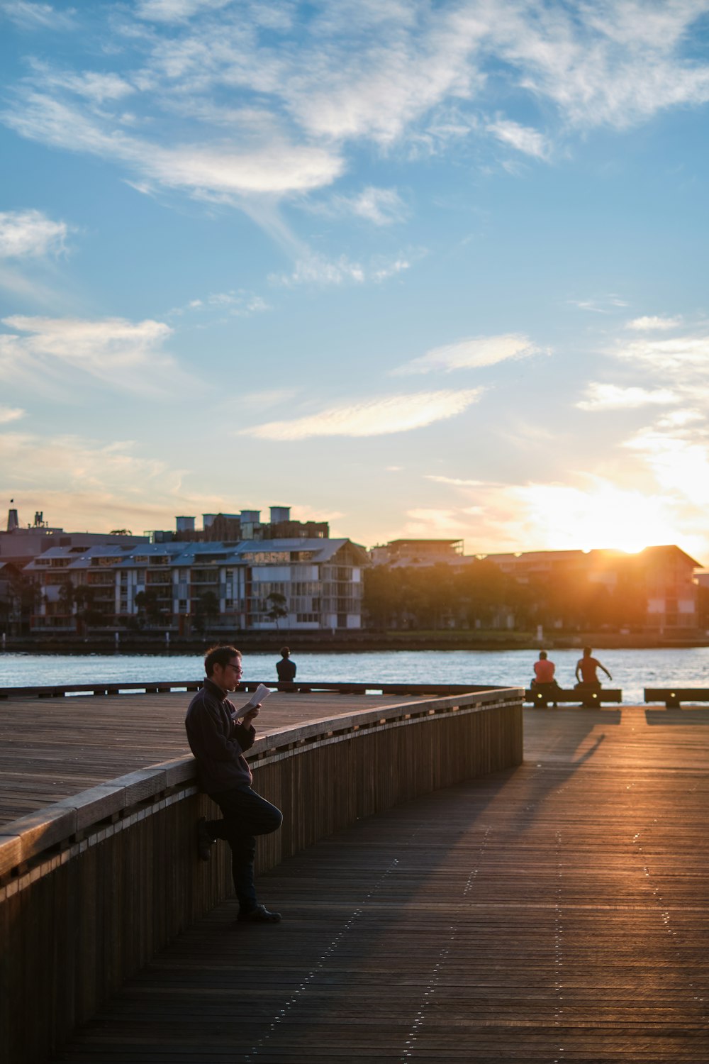 man in black jacket sitting on brown wooden dock during sunset