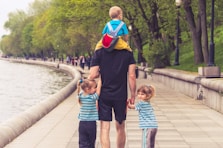 man in black t-shirt and brown shorts holding girl in blue and black jacket walking