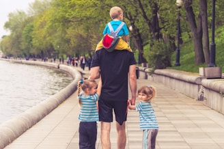 man in black t-shirt and brown shorts holding girl in blue and black jacket walking