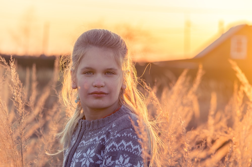 girl in blue and white floral shirt standing on brown grass field during daytime