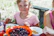 A happy young woman enjoying a colorful fruit mix snack outdoors on a sunny day.
