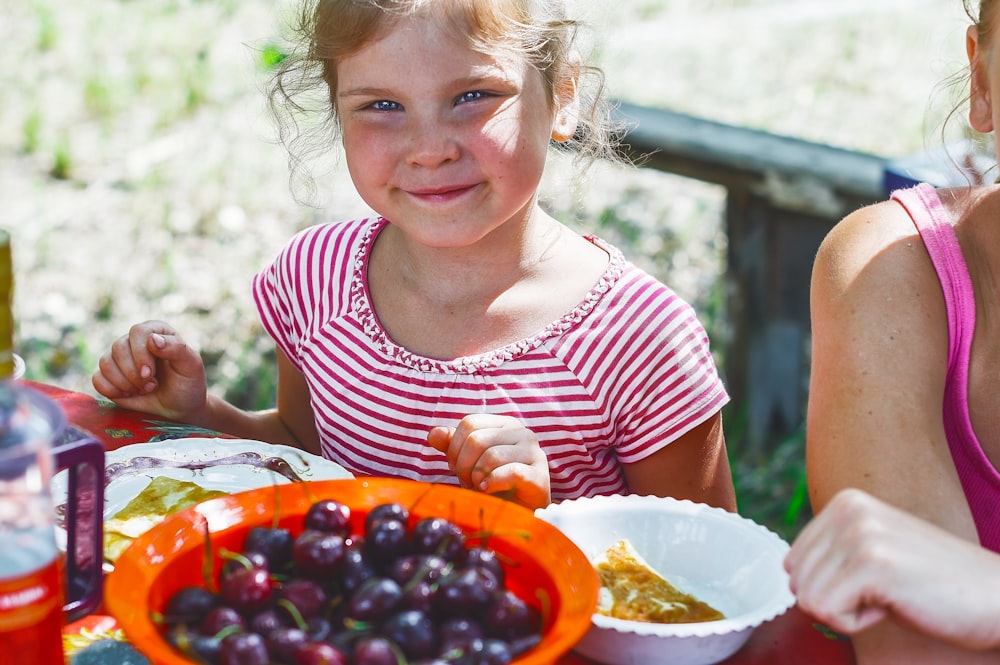 girl in red and white striped shirt holding white ceramic bowl with red and black fruits