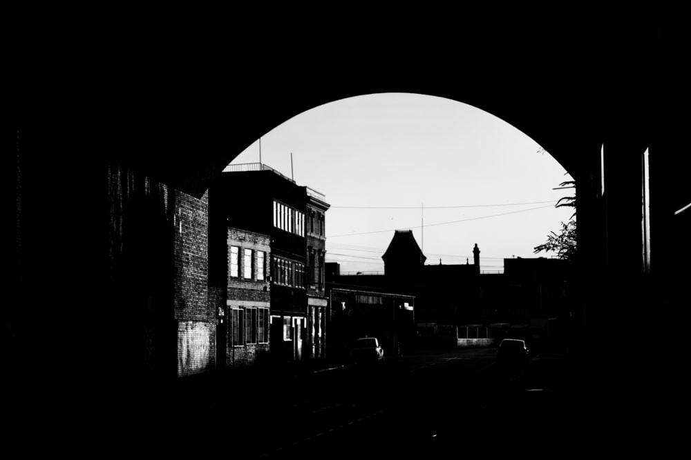 grayscale photo of a city with cars parked on the side of the road