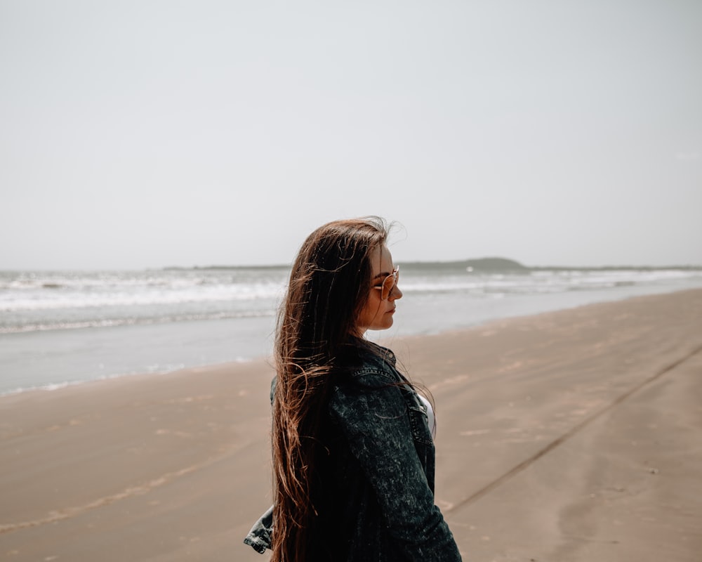昼間のビーチに立つ黒いデニムジャケットの女性