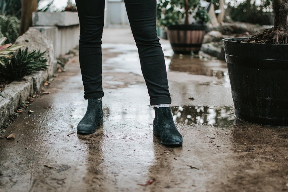 person in black pants and black leather boots standing on gray concrete floor