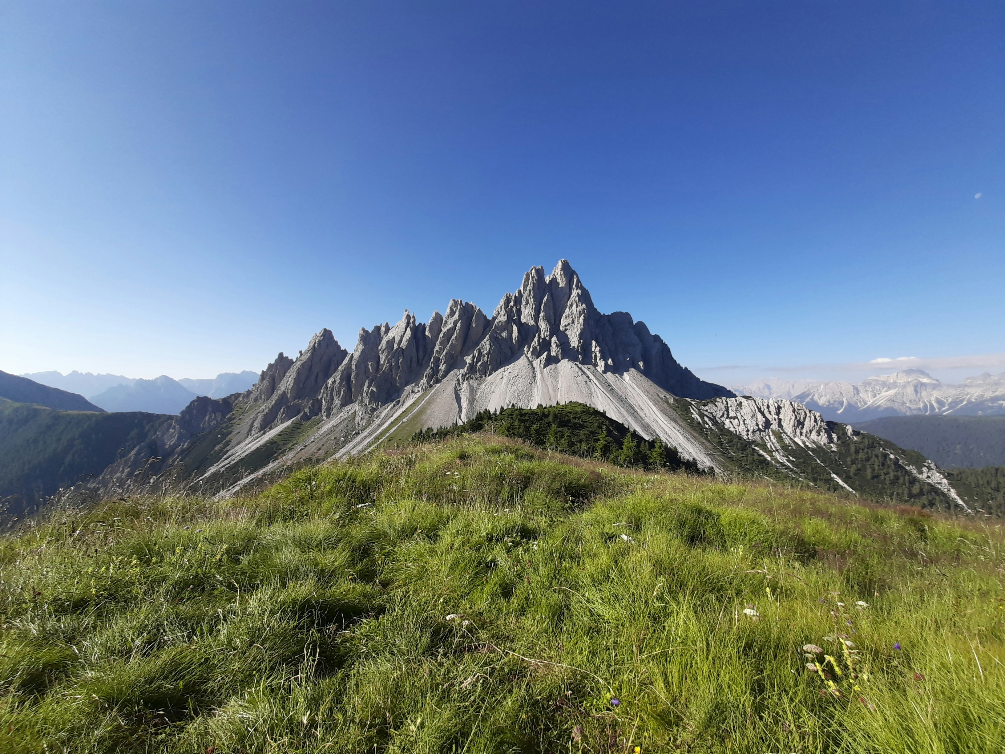 green grass field near mountain under blue sky during daytime