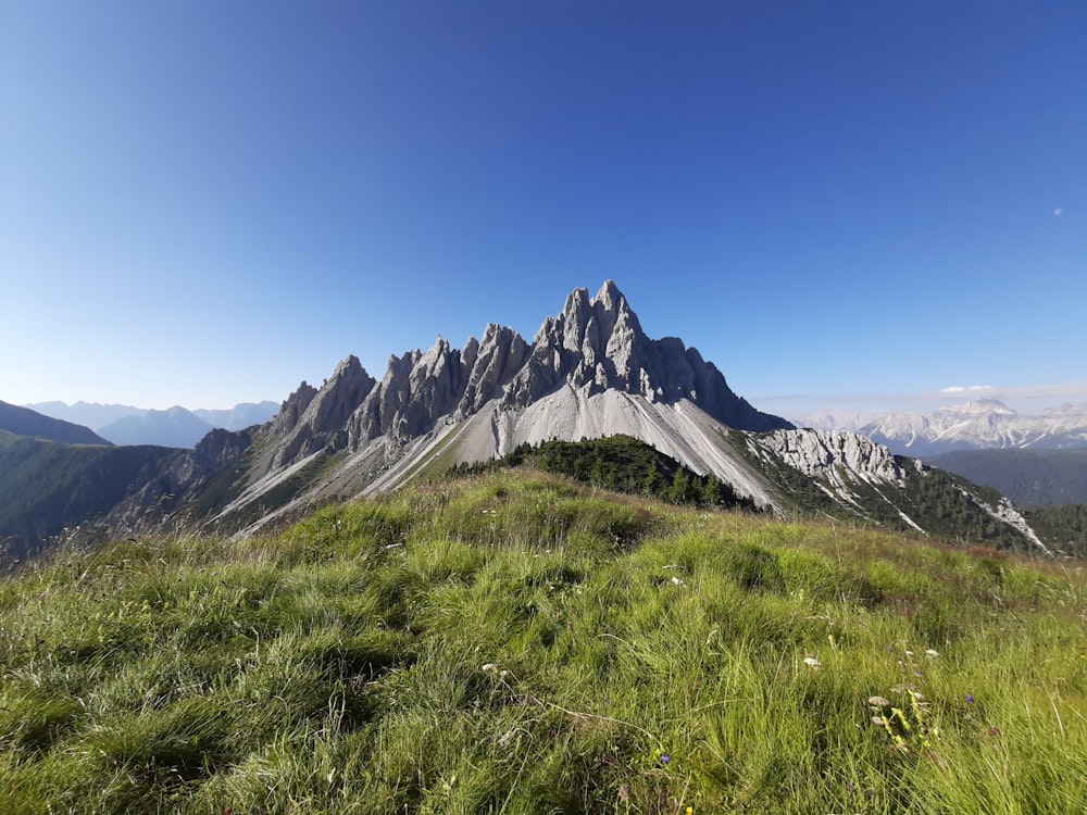 green grass field near mountain under blue sky during daytime