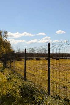 grey metal fence near green grass field during daytime