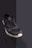 A single black athletic shoe with a white sole is positioned against a plain, dark background. The shoe has visible wear and tear, including scuffs and dirt marks, particularly on the toe area. The laces appear loose, and the shoe is slightly angled to show its front and side.