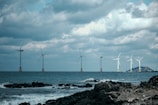 Engineers setting up tidal energy equipment along a rocky shoreline under cloudy skies.