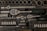 A collection of various metal tools neatly organized in a black foam case. Included are ratchets, sockets, and other attachments, each in their designated slot. The tools appear to be primarily made of metal, with some having rubberized handles.