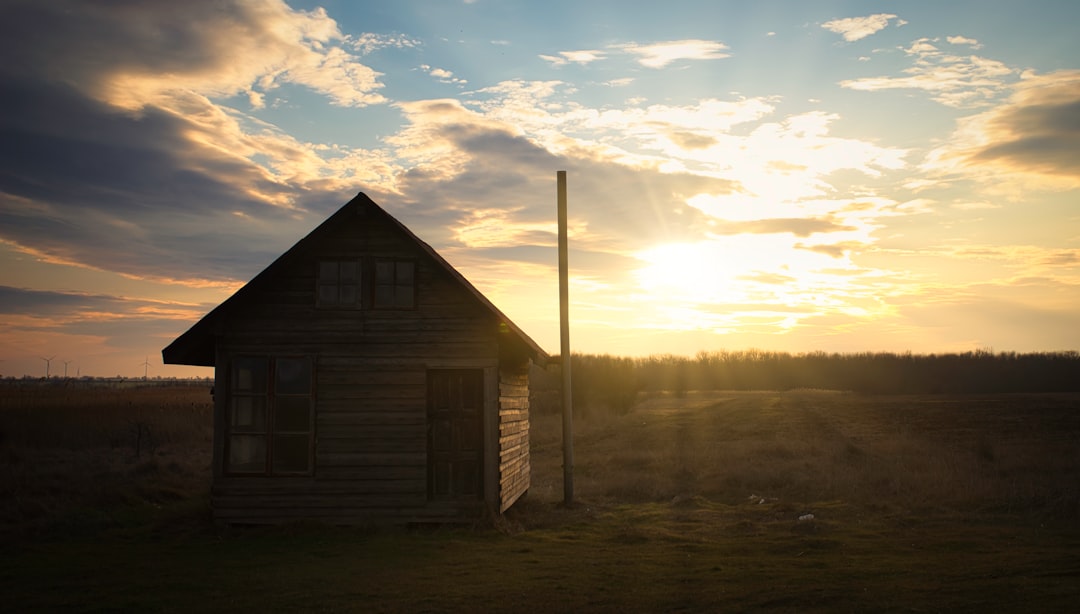 brown wooden house near trees under white clouds and blue sky during daytime