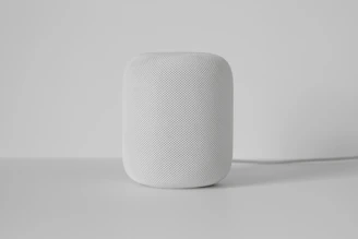 A modern smart home assistant device sitting on a white shelf surrounded by minimal décor.