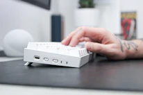 Close-up of hands typing on a mechanical keyboard surrounded by manga volumes and gaming accessories.