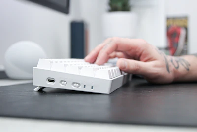 Close-up of hands typing on a mechanical keyboard surrounded by manga volumes and gaming accessories.