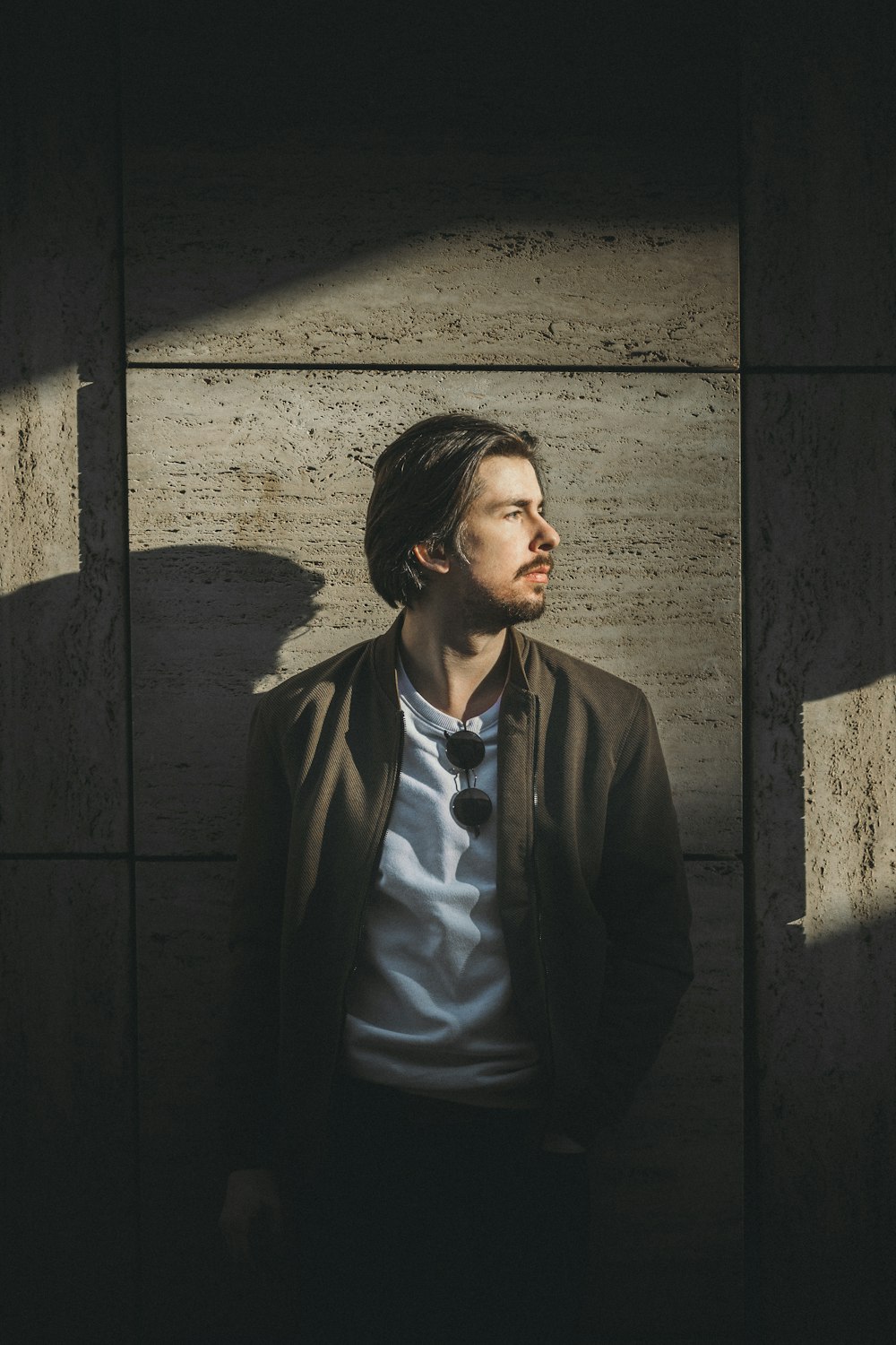 man in black suit jacket standing beside gray concrete wall