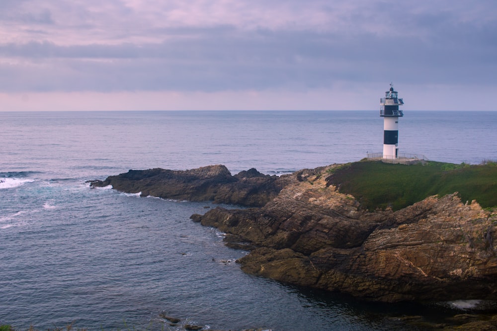 white and brown lighthouse on brown rock formation beside sea during daytime