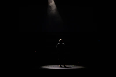 An actor rehearsing a dramatic monologue under warm spotlight on a dark stage.